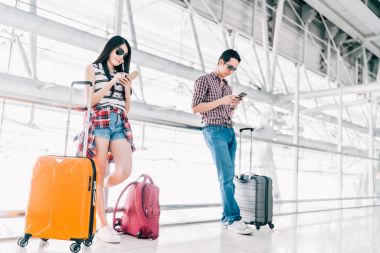 Genç Asyalı erkek ve kadın uçuş veya online check-in sırasında Havaalanı Bagaj ile birlikte kontrol smartphone kullanarak. Hava yolculuğu, yaz tatili veya cep telefonu uygulama teknoloji kavramı