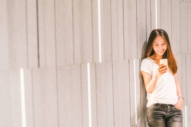 Smartphone kullanarak ve gülümseyen genç güzel Asyalı kız ya da üniversite öğrencisi. Modern yaşam tarzı, mobil iletişim teknolojisi, gündelik iş veya eğitim kavramı