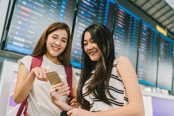 Två Asiatiska Tjejer Använder Smartphone Tillsammans Flight Information Styrelsen Flygplats — Stockfoto
