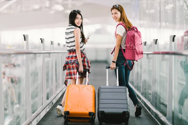 Två glada Asiatiska tjejer reser utomlands tillsammans, bära resväska bagage på flygplatsen. Flygresor eller semester semester koncept — Stockfoto