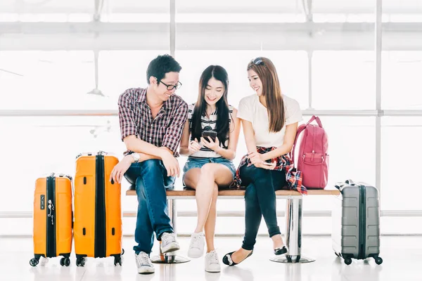 Gruppen av unga asiatiska resenärer med smartphone kontrollerar flyg eller online incheckning på flygplats tillsammans med bagage. Resa utomlands, sommaren semesterresa eller mobiltelefon ansökan teknik koncept — Stockfoto