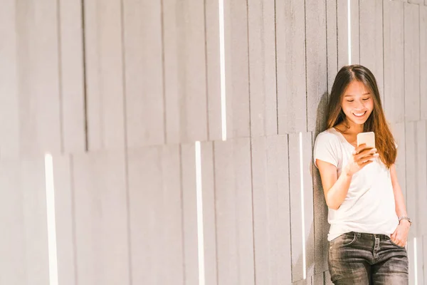 Joven hermosa chica asiática o estudiante universitaria usando teléfono inteligente y sonriendo. Estilo de vida moderno, tecnología de comunicación móvil, negocios casuales o concepto educativo —  Fotos de Stock