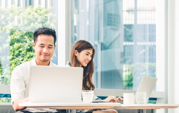 Jovem casal asiático ou estudante universitário usando notebook de computador portátil trabalham juntos em uma cafeteria ou campus universitário. Tecnologia da informação, estilo de vida do café, reunião de escritório ou conceito de e-learning — Fotografia de Stock