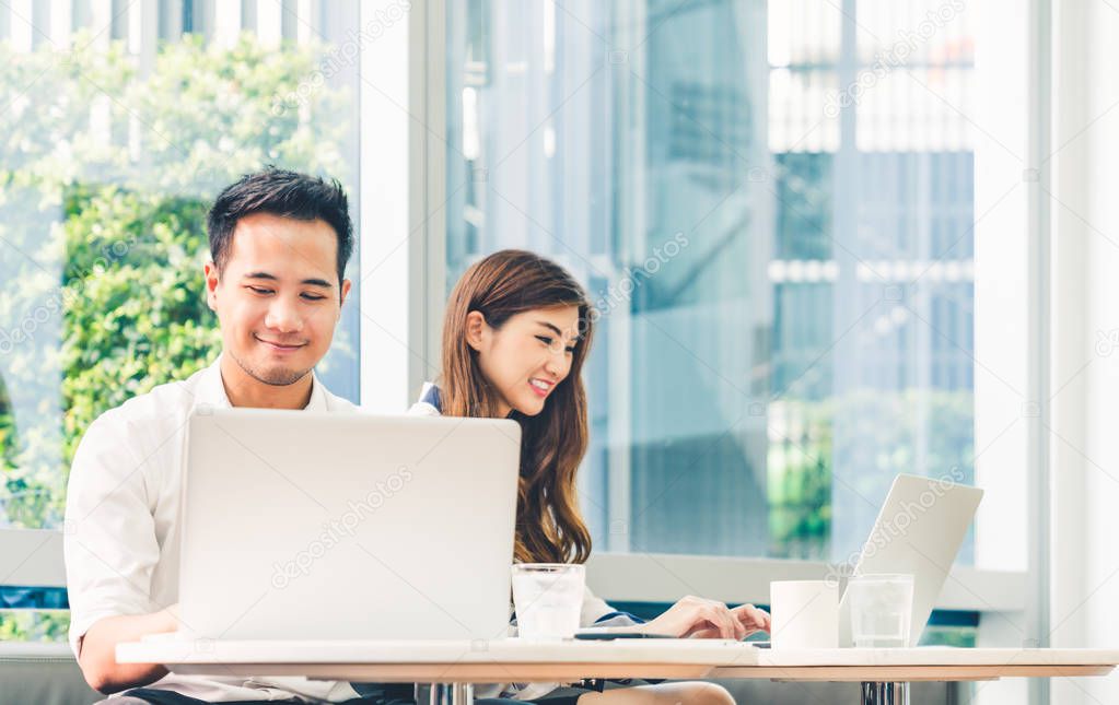 Young Asian couple or college student using laptop computer notebook work together at coffee shop or university campus. Information technology, cafe lifestyle, office meeting, or e-learning concept