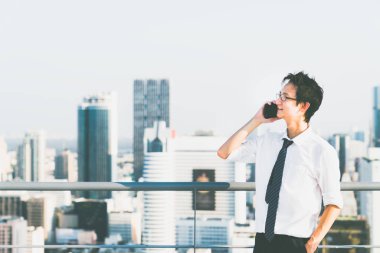 Bina çatı, şehir görünümü arka plan üzerinde kopya alanı üzerinde hareket eden telefon çağrısıyla genç Asya iş adamı. İş iletişimi, ticari faaliyet, telefonla satış veya office çalışan yaşam tarzı kavramı