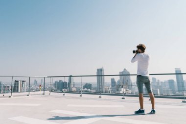 Genç Beyaz çatı güneşli günde bina cityscape fotoğrafta beyaz adam. Fotoğrafçılık hobi, Gadget'ı teknoloji veya boş zaman etkinliği konsepti. Mavi gökyüzü ile kopya alanı