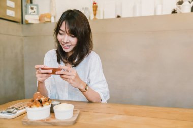Güzel Asyalı kız alarak fotoğraf çikolatalı tost pasta, dondurma ve süt kahve dükkanında. Tatlı veya gıda fotoğraf hobi. Akıllı telefon veya cep telefonu fotoğraf alışkanlık kavramı. Kopya alanı ile