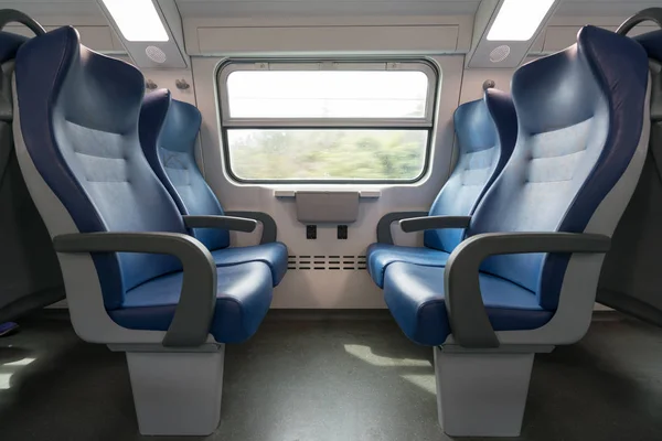 Четыре пустых синих сиденья лицом друг к другу в современном европейском поезде. Железнодорожные поездки или транспортная концепция — стоковое фото