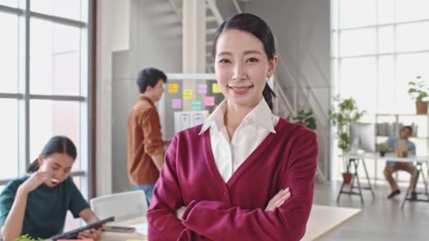 Portrait panoramique 4K de belle femme asiatique souriante, bras croisés dans un bureau moderne, jeune équipe créative travaillant ensemble en arrière-plan. Leader féminin, PDG d'entreprise, ou concept de propriétaire d'entreprise 