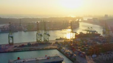 Kargo konteynırı nakliye gemisi ve vinç Singapur sanayi bölgesinde, siluet günbatımı. Lojistik sektörü, nakliye işi konsepti. İHA yüksek açı görüntüsü taraması