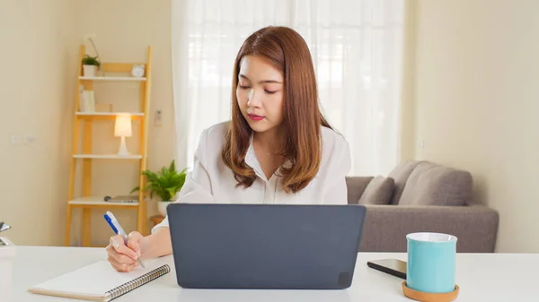 Young adult Asian woman work at home or modern office, using notebook laptop computer. Work from home life, information technology, domestic lifestyle, or self isolation remote working concept