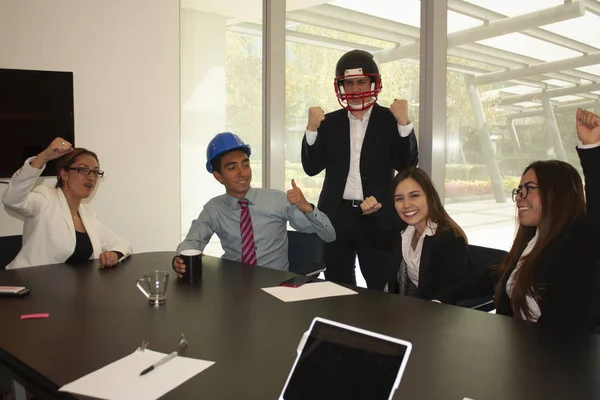 Work team excited about the attitude of its leader who wears an American helmet to empower the team in offices in Mexico City