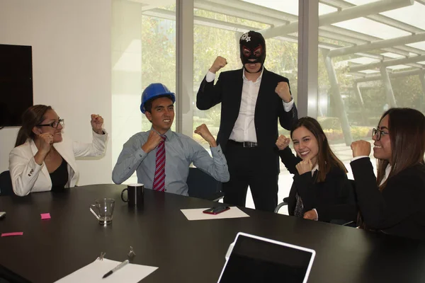 Boss in the office wearing a wrestler mask moves to the team enthusiasm the architect and his companions are motivated and laugh accepting challenges and relaxing, the work team raises their fists demonstrating a winning attitude