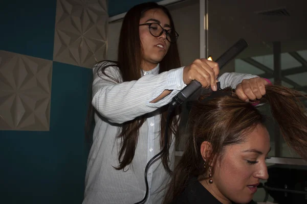 Straight hair stylist woman uses pincer beauty tools and brush using her hands to comb and stylize the amber hair of a brunette woman in Mexico
