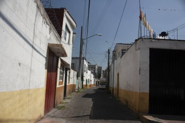 Mexico City 'deki kaldırım taşı sokakta iki renkli beyaz ve sarı cephelerin arasında asılı elbiseler de var.