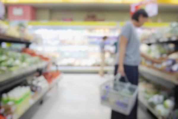 Fondo abstracto borroso de las personas que compran en el supermercado con productos diversos en los estantes — Foto de Stock