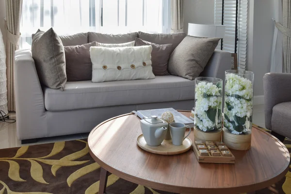 decorative tea set and glass vase on wooden round table in living room interior