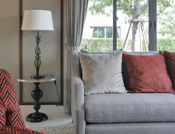 Moderno diseño de la sala de estar con almohadas rojas en el sofá y lámpara de mesa decorativa — Foto de Stock