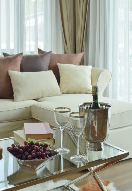 Şarap, gözlük ve bej kanepe modern klasik oturma odasında koyu kahverengi yastık ile masada şarap şişesi