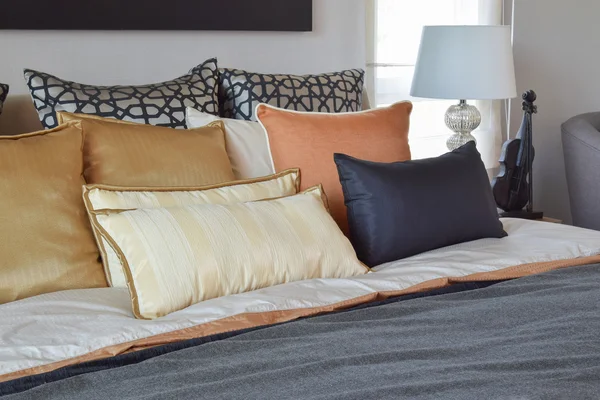 Modern bedroom interior with orange and gold pillows on bed and bedside table lamp — Stock Photo, Image