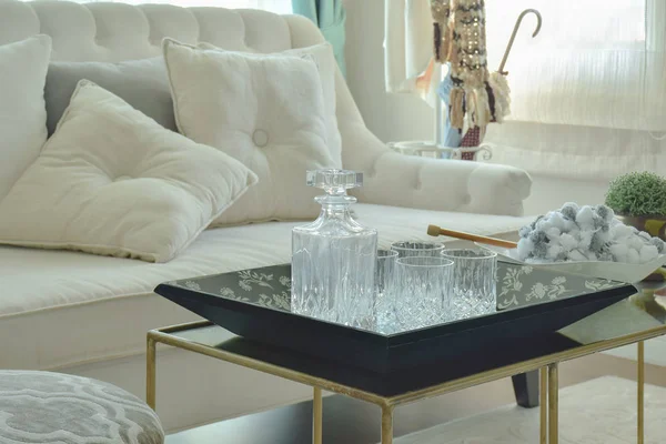 Botella de cristal y vasos sobre mesa con sofá beige en salón — Foto de Stock