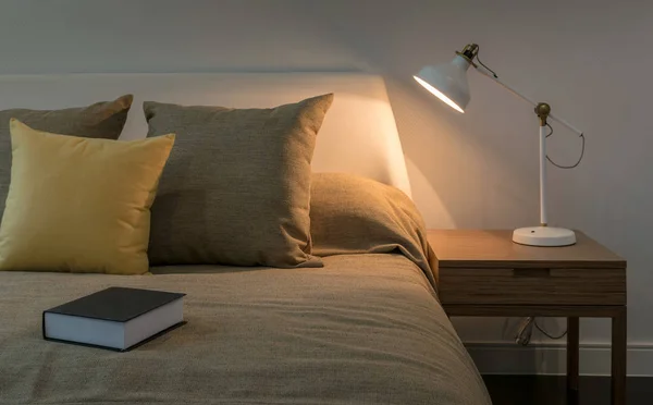 Interior acolhedor quarto com livro e lâmpada de leitura na mesa de cabeceira — Fotografia de Stock