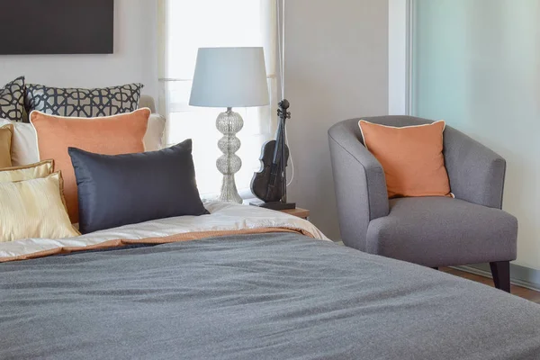 Сучасний інтер'єр спальні з помаранчевою подушкою на сірому стільці і настільна лампа вдома — стокове фото