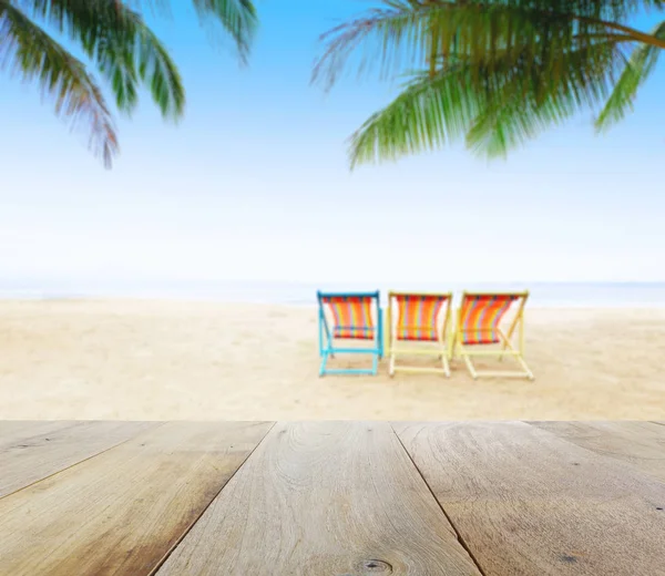 Mesa de madera sobre fondo borroso playa con sillas de playa bajo el cocotero — Foto de Stock