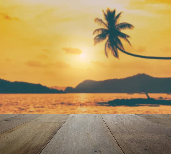 Mesa de madera con coco borroso colgando sobre la playa tropical al atardecer — Foto de Stock