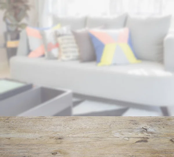 Mesa de madera con desenfoque de diseño moderno de la sala de estar con almohadas de colores en el sofá — Foto de Stock