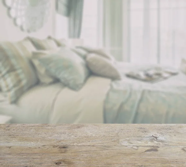 Mesa de madera con desenfoque interior del dormitorio con almohadas y decorativo conjunto en la cama — Foto de Stock