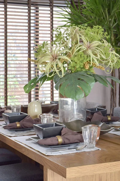 Велика красива ваза з зеленою квітковою обстановкою з сучасним обіднім набором на дерев'яному столі — стокове фото