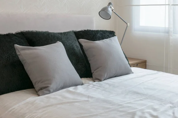 Интерьер спальни с серыми подушками на белой кровати и декоративной настольной лампой . — стоковое фото