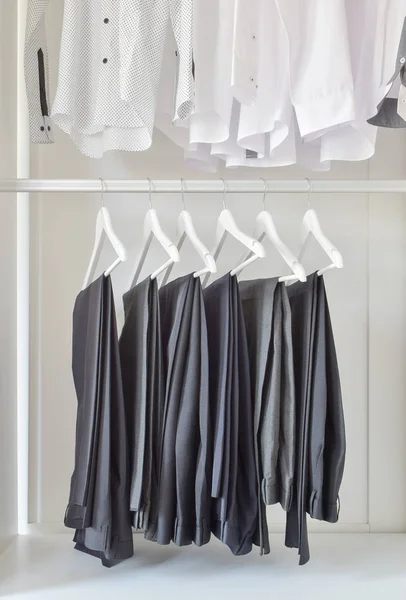 Linha de camisas brancas e calças pretas penduradas em guarda-roupa de madeira — Fotografia de Stock
