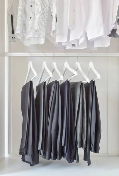 Rij van witte shirts en zwarte broek hangen in houten kast — Stockfoto