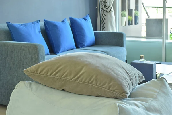 Almohada marrón sobre taburete cúbico de tela beige con sofá azul en el fondo — Foto de Stock