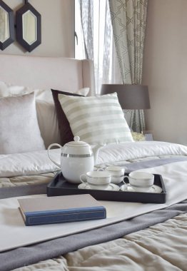 Kitap ve modern yatak odasında yatağın üstüne çay seti ile dekoratif tepsi