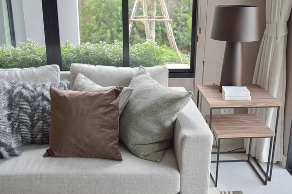 Almohadas marrones y grises claros colocados en sofá beige en la esquina de la sala de estar — Foto de Stock