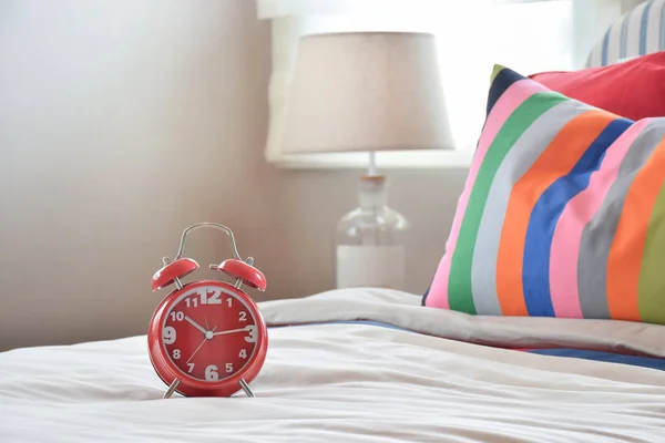 Red clock on white blanket and colourfull striped pillows — Stock Photo, Image
