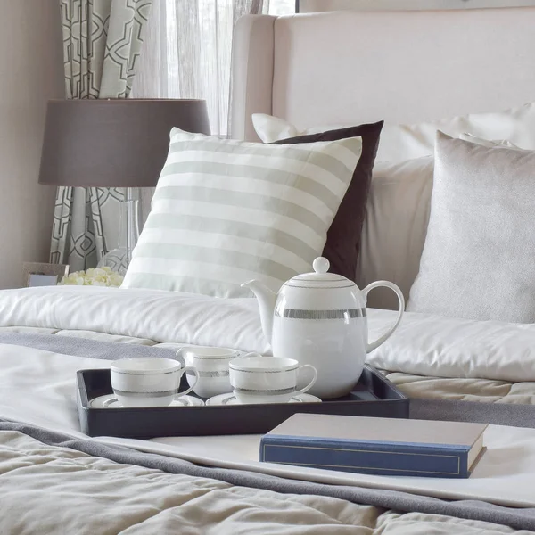 Декоративный поднос с книгой и чайным сервизом на кровати в современной спальне — стоковое фото