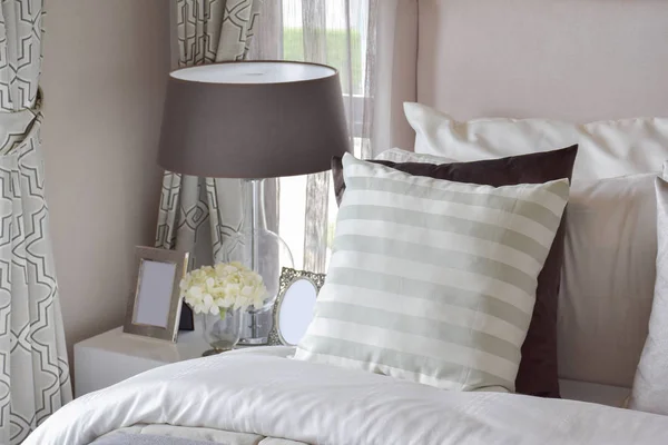 Современный интерьер спальни с зеленой полосатой подушкой на кровати и прикроватный светильник на дому — стоковое фото