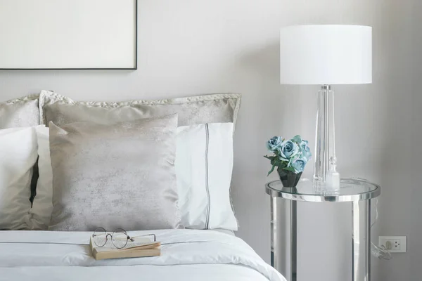 Almohadas de color gris claro y blanco en la cama con tarro de flores en la mesita de noche —  Fotos de Stock