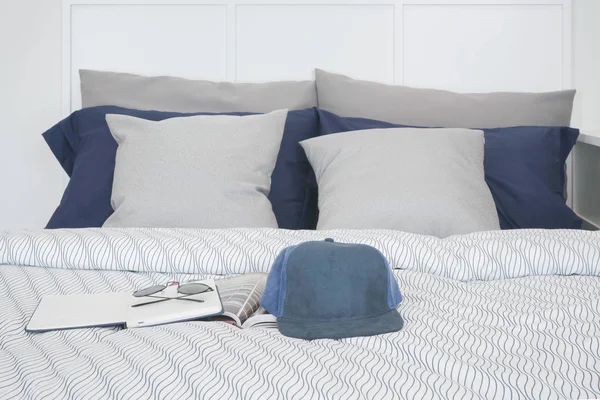 Boné, caderno e óculos de sol na cama com travesseiros no fundo — Fotografia de Stock