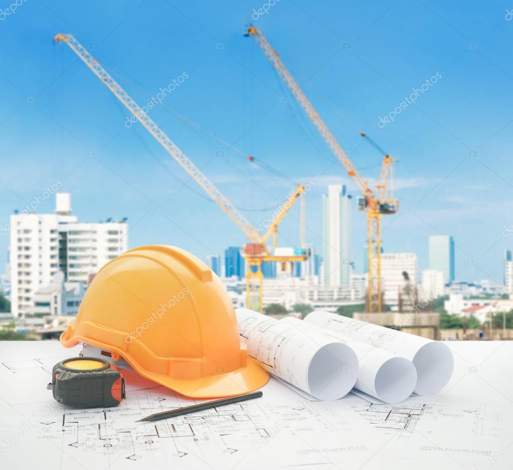 architectural blueprint with safety helmet and tools over construction site