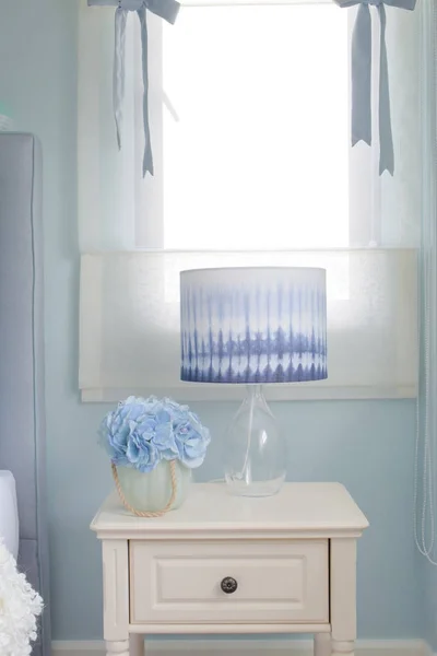 Flower jar and reading lamp on bedside table in light blue interior bedroom — Stock Photo, Image