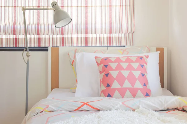 Corallo rosa triangolo modello cuscino impostazione sul letto con lampada da lettura pieghevole accanto al letto — Foto Stock