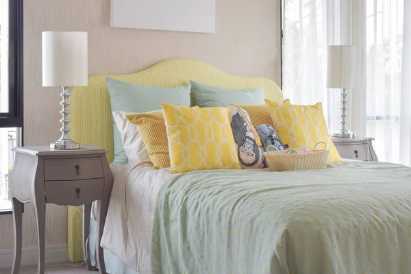 Classic style bedside table with reading lamp next to cozy style bedding with many style of green and yellow pillows — Stock Photo, Image