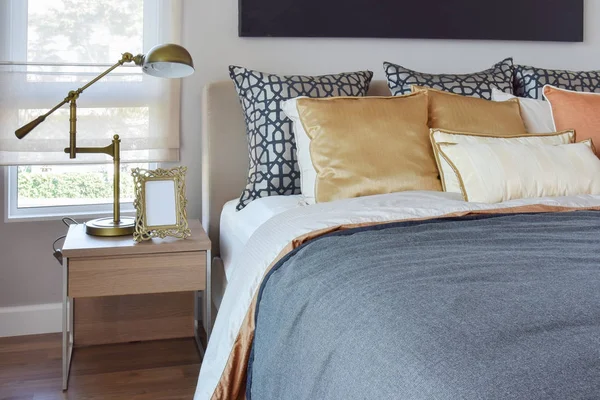 Modern bedroom interior with orange and gold pillows on bed and bedside table lamp — Stock Photo, Image