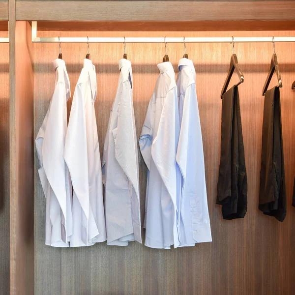 Row of white shirts and black pants hanging in wooden wardrobe — Stock Photo, Image