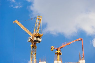 İnşaat alanında mavi gökyüzü ve bulutlar üzerinde kule vinç ve beton pompası